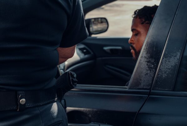 A police officer issuing a ticket to a man seated in a car, captured outdoors in daylight.