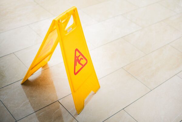 A bright yellow caution sign on a tiled floor indicates a wet surface, alerting passersby to potential hazards.
