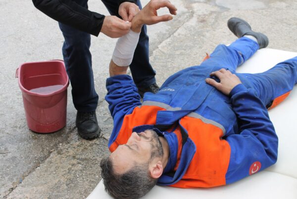 Injured worker receiving first aid on-site with arm bandage applied.
